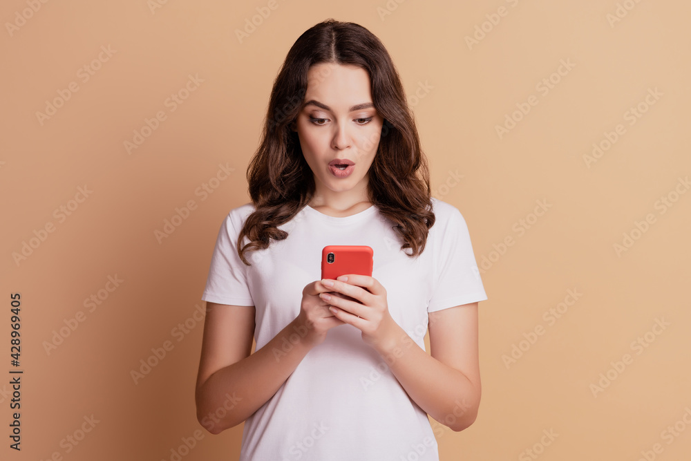 Photo of amazed surprised girl hold phone look screen open mouth posing on beige background Photo of amazed surprised girl hold phone look screen open mouth posing on beige background