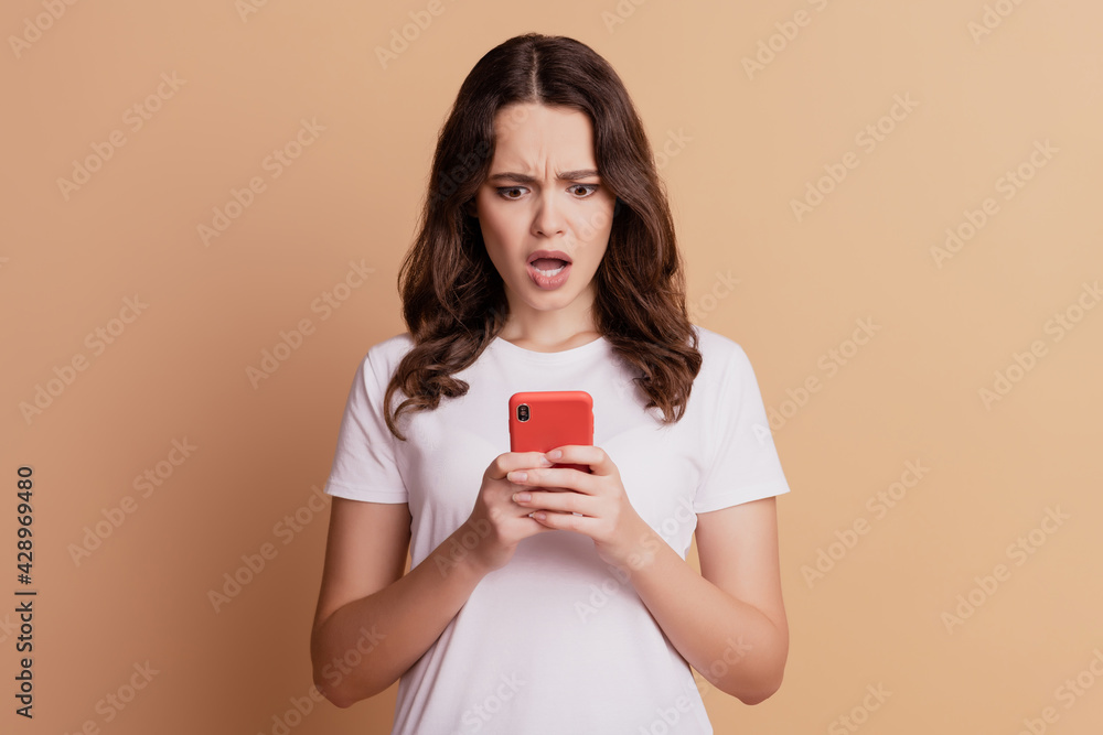 Photo of crazy shocked lady hold smartphone look screen open mouth posing on beige background Photo of crazy shocked lady hold smartphone look screen open mouth posing on beige background