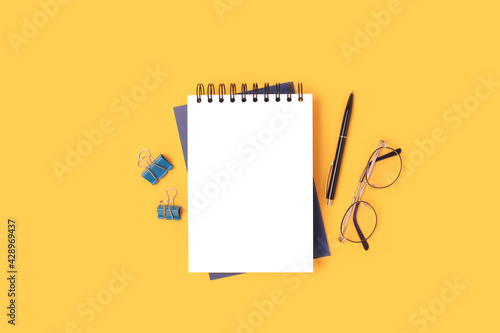 Workspace with notepad mockup, eyeglasses and stationery on a yellow background. School concept with copyspace.