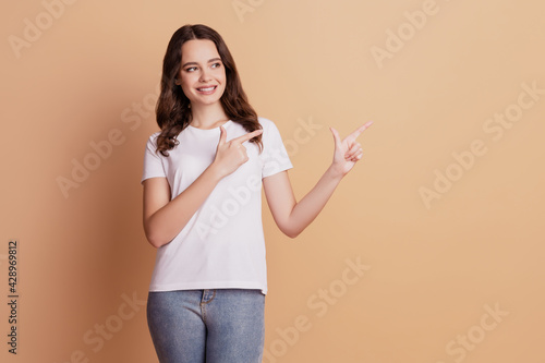 Portrait of positive pretty girl indicate fingers empty space isolated on beige background