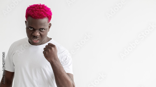 Brutal man. Black lives matter. Threaten gesture. Straggle opposition. Social pressure. Advertising background. Aggressive african guy with pink hair clenching fist isolated white copy space. photo