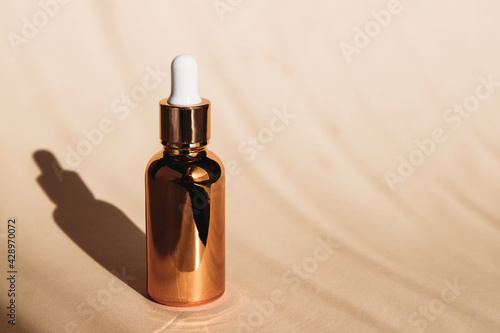 A golden jar of serum or hyaluronic acid in the bright summer sun. Facial skin care and moisturizing. Hard shadows. Place for text