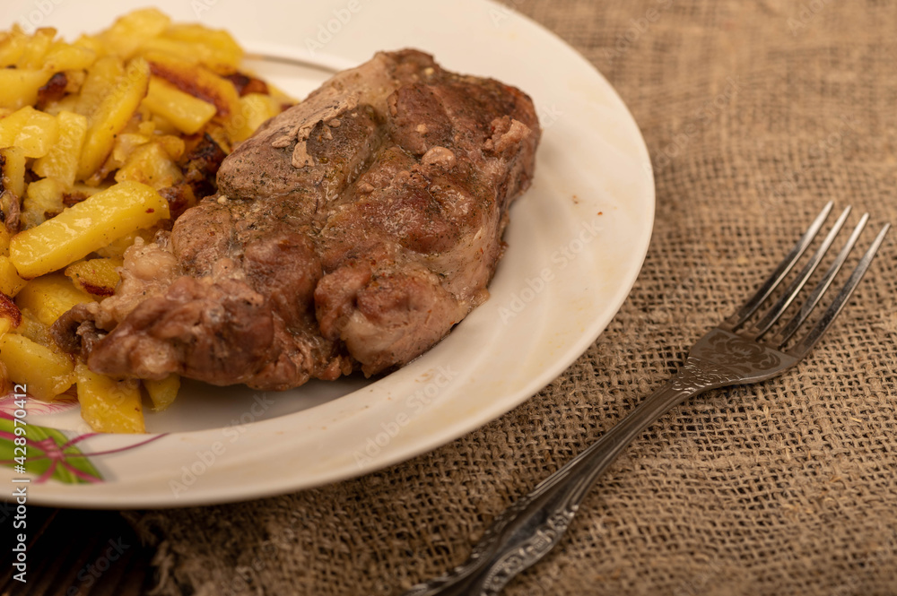 Homemade fried potatoes and a large piece of meat on a white plate. Homemade fried potatoes and a large piece of meat on a white plate.