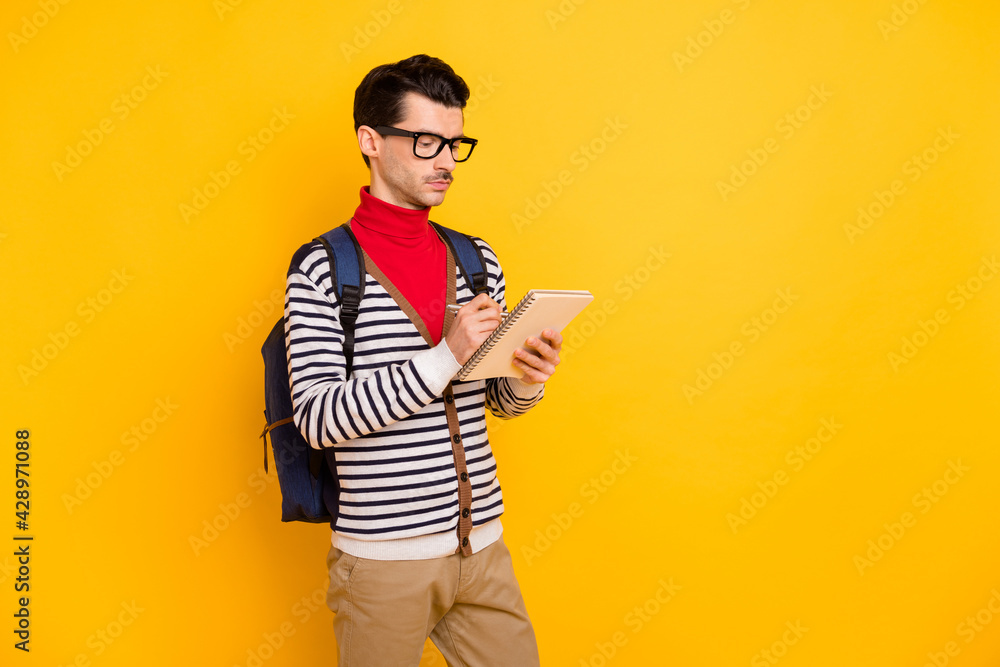 Profile side photo of young guy serious write notebook plan to-do list homework study backpack isolated over yellow color background Profile side photo of young guy serious write notebook plan to-do list homework study backpack isolated over yellow color background