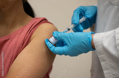 Nurse  doctor or General practitioner in blue gloves holding syringe  making injection or vaccination to young female patient in red shirt in clinic. Covid-19 or coronavirus vaccine  with copy space