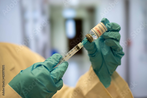 Doctor, nurse dials coronavirus vaccine from an ampoule into a syringe, with blurred hospital background.