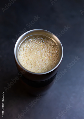 Coffee and vegetable oat coconut almond milk foam at thermos metal cup, top view