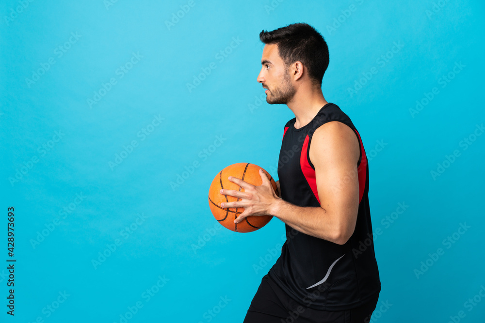 Young handsome man isolated on blue background playing basketball