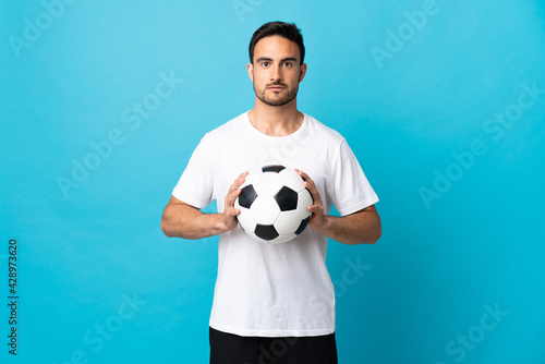 Young handsome man isolated on blue background with soccer ball