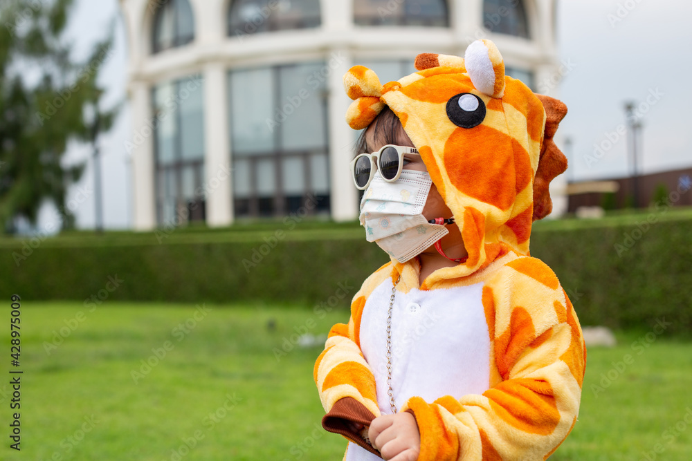 Fototapeta premium A cute Asian girl wearing a giraffe costume, Sunglasses travel in a new normal state with a face mask.