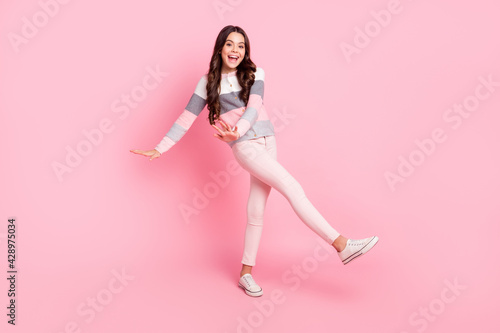 Full size photo of young lovely smiling cheerful little girl in striped sweater dancing isolated on pink color background