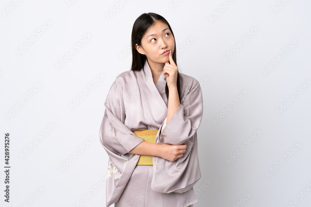 Young Chinese girl wearing kimono over isolated background having doubts while looking up Young Chinese girl wearing kimono over isolated background having doubts while looking up