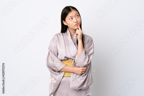 Young Chinese girl wearing kimono over isolated background having doubts while looking up