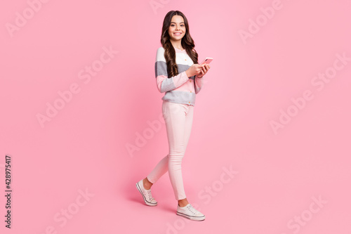 Full size of charming attractive little girl hold phone walk empty space isolated on pastel pink color background © deagreez