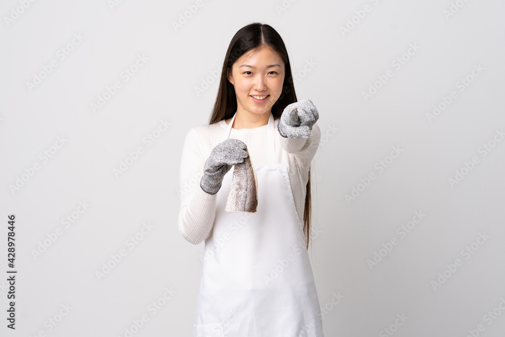 Chinese fishmonger wearing an apron and holding a raw fish over isolated white background pointing front with happy expression Chinese fishmonger wearing an apron and holding a raw fish over isolated white background pointing front with happy expression