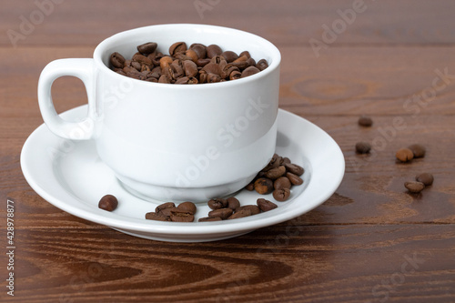 white cup, saucer and coffee beans on a wooden background