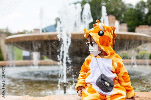 Fototapeta Naklejka Na Ścianę i Meble -  A cute Asian girl wearing a giraffe costume, Sunglasses travel in a new normal state with a face mask.