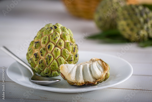 Sugar apple on a white plate with stainless steel spoon, ready to be eaten on an aged white wooden table. photo