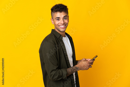 Young brazilian man isolated on yellow background sending a message or email with the mobile