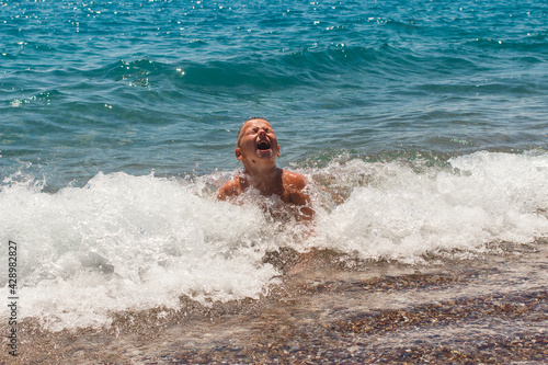Nine-year-old tanned boy plays on the waves by the sea