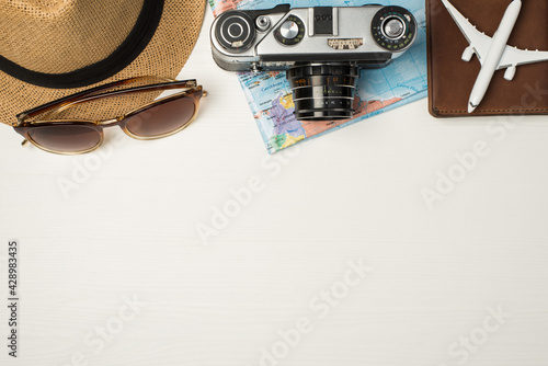 Top view photo of sunglasses headwear camera map and plane model on passport cover on isolated wooden white background with copyspace
