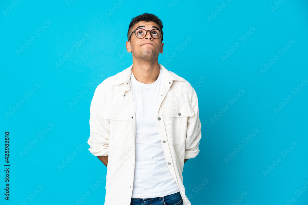 Young Brazilian man isolated on blue background and looking up Young Brazilian man isolated on blue background and looking up