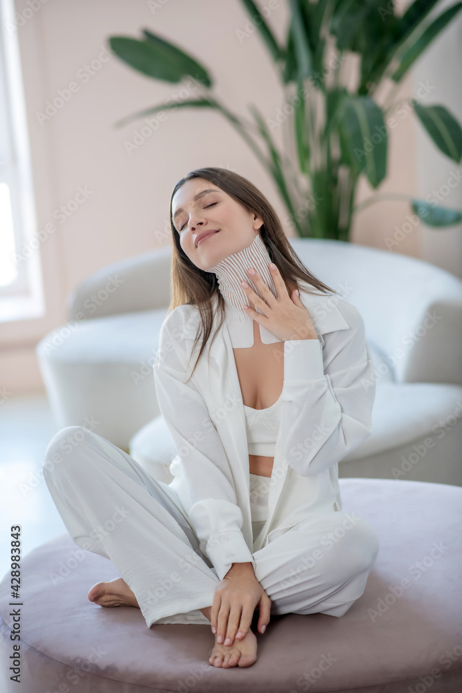 Young woman in white sitting on a round chair with tapes on her neck Young woman in white sitting on a round chair with tapes on her neck