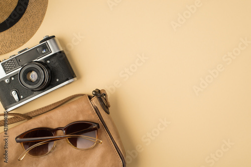 Top view photo of cap camera and sunglasses on leather bag on isolated beige background with copyspace