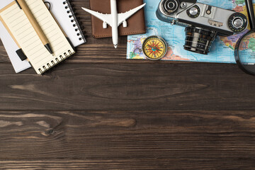 Top view photo of plane model on passport cover magnifier camera and compass on map notebooks pen on isolated wooden table background with copyspace