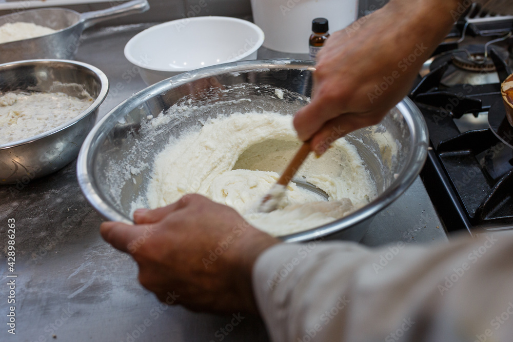 Pasticciere specializzato mentre lavora l'impasto di un dolce con ricotta in una bull d'acciaio Pasticciere specializzato mentre lavora l'impasto di un dolce con ricotta in una bull d'acciaio
