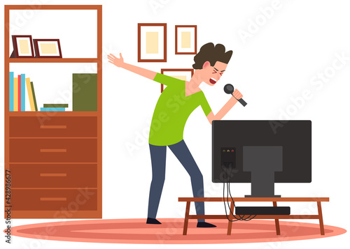 Man holding microphone and singing in karaoke to music. Boy stands with mike next to TV at home