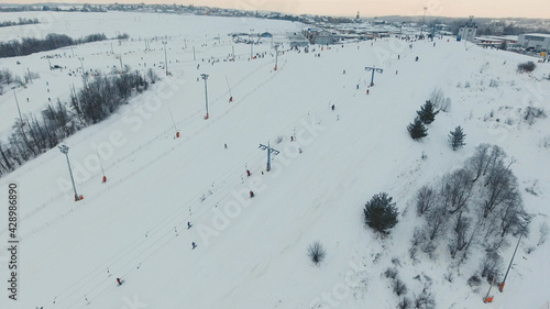 Aerial view: Skiers and snowboarders going down the slope in winter day. Skiers and snowboarders enjoying on slopes of ski resort in winter season.