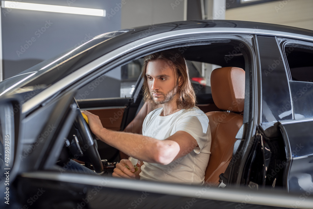 Serious man in car salon wiping steering wheel