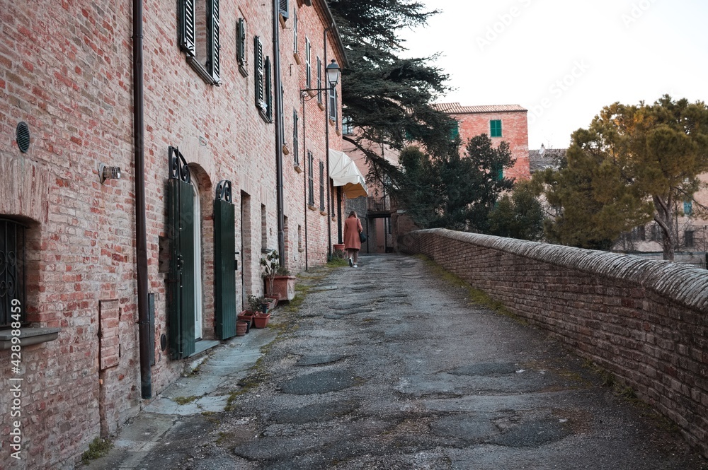 An alley of a medieval village with ruined brick houses and a walking tourist (Corinaldo, Marche, Italy)