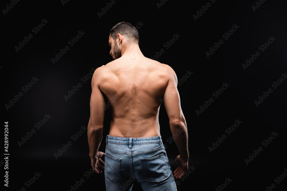 back view of shirtless, muscular man in jeans on black background.