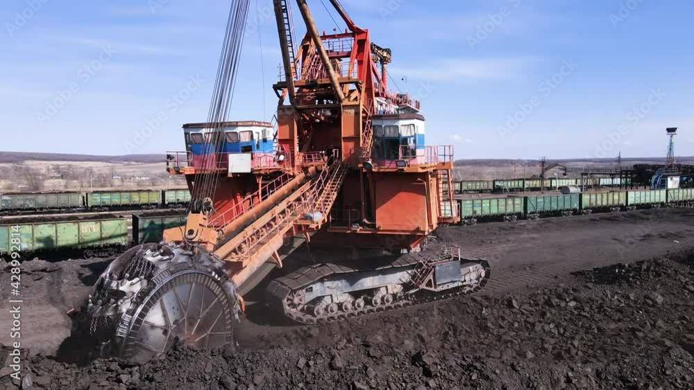 Open pit coal mining. Large mining equipment picks up coal from the warehouse with a bucket. Loading coal into railway cars. Open pit coal mining. Large mining equipment picks up coal from the warehouse with a bucket. Loading coal into railway cars.