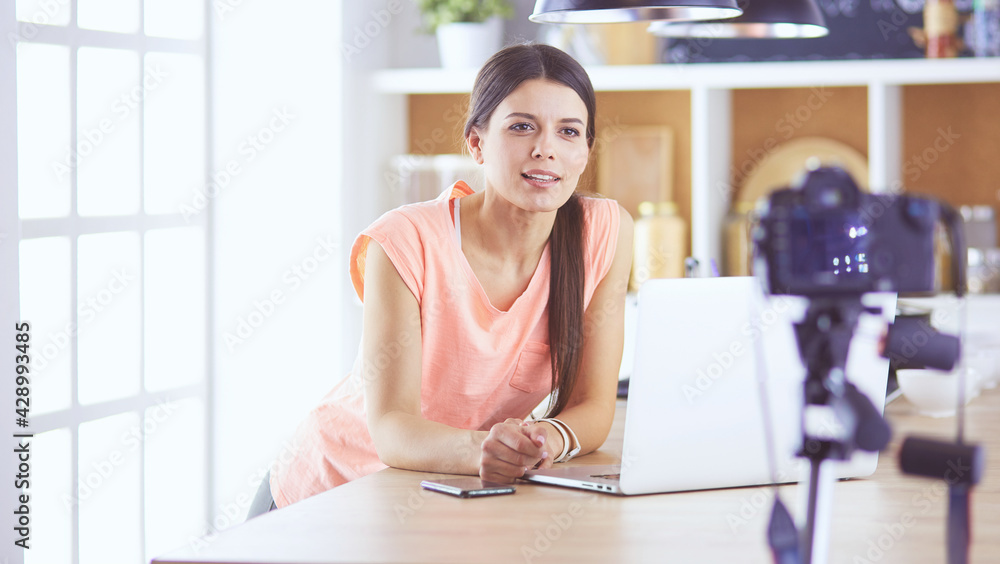 Obraz premium Young woman in kitchen with laptop computer looking recipes, smiling. Food blogger concept