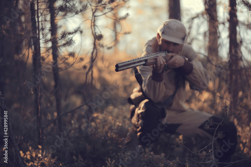 hunting man / hunter with a gun hunting in the autumn forest, yellow trees landscape in the taiga