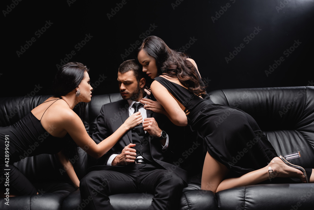 sexy, elegant women seducing businessman sitting on leather couch on black.  Stock Photo | Adobe Stock