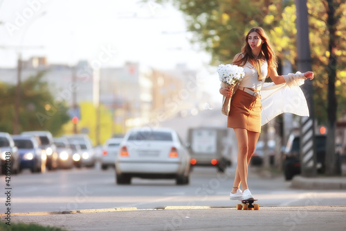 girl riding a skate in the city / model young adult girl on the street in full growth, board on wheels