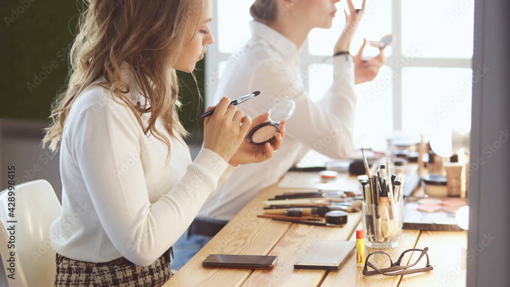 Make-up artist applying white eyeshadow in the corner of model's eye and holding a shell with eyeshadow on background Make-up artist applying white eyeshadow in the corner of model's eye and holding a shell with eyeshadow on background