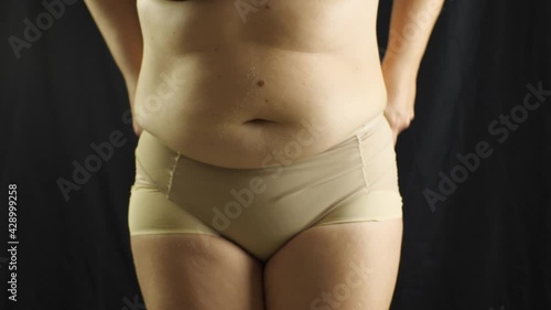 The chubby girl takes off her corrective panties, hiding figure flaws. Black background