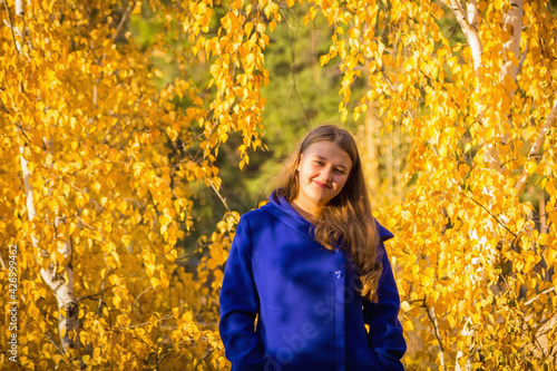 A young girl walks in the autumn park  stands behind a tree.
