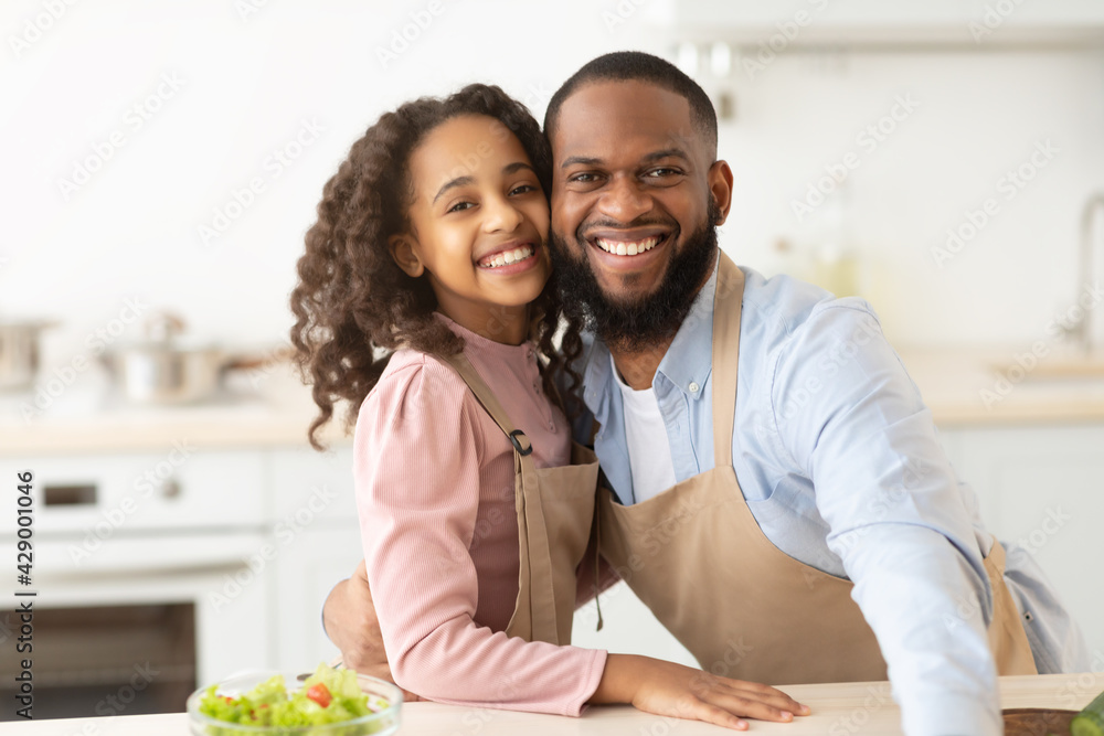 Cheerful black father and daughter posing in kitchen Cheerful black father and daughter posing in kitchen