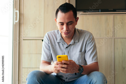 Hispanic Man using cellular phone while sitting in living room