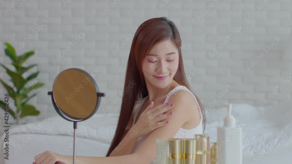 Happy Asian young woman smile and looking in mirror doing skin care applying lotion on her shoulder and beauty treatment at home,Wellness girl self care with beauty product at home Happy Asian young woman smile and looking in mirror doing skin care applying lotion on her shoulder and beauty treatment at home,Wellness girl self care with beauty product at home