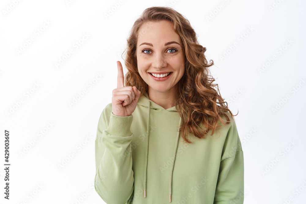Portrait of beautiful blond girl smiling, pointing finger up at top, showing promo text, display a link to click, standing over white background Portrait of beautiful blond girl smiling, pointing finger up at top, showing promo text, display a link to click, standing over white background