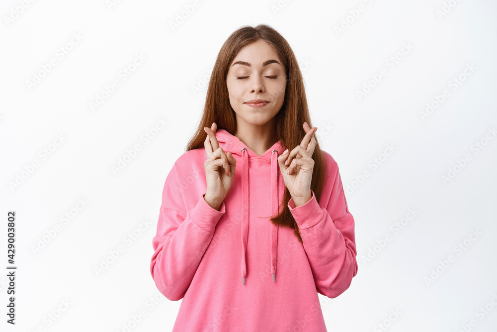 Young hopeful teen girl close eyes, smile and cross finger for good luck, praying or making wish, anticipating good news, standing over white background Young hopeful teen girl close eyes, smile and cross finger for good luck, praying or making wish, anticipating good news, standing over white background