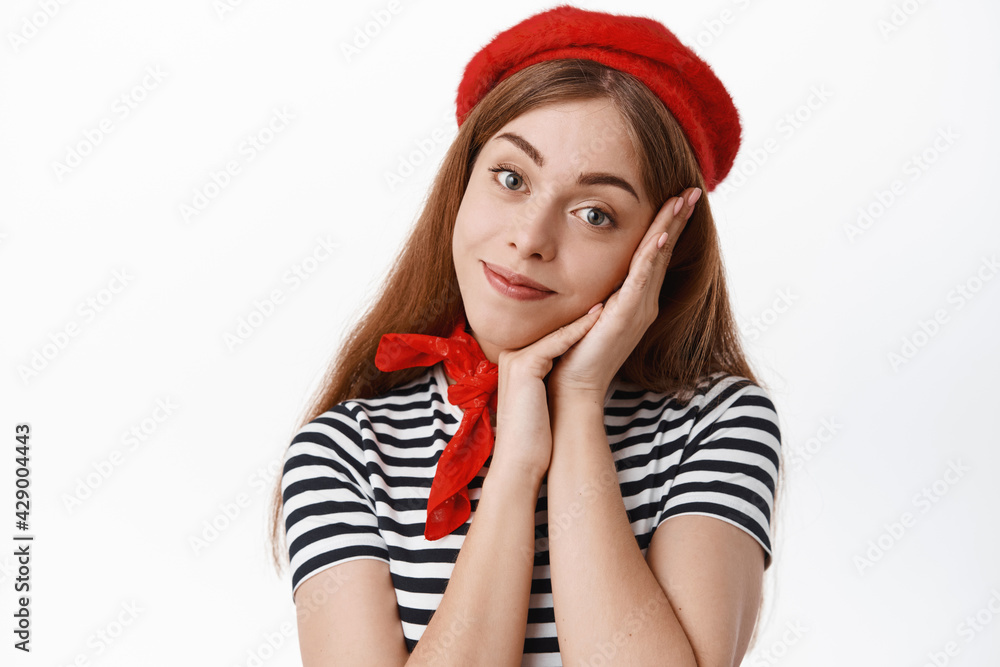 Beautiful lady in red beret, lean face on palm and smile at camera with romantic expression, gazing at you or daydreaming, standing against white background Beautiful lady in red beret, lean face on palm and smile at camera with romantic expression, gazing at you or daydreaming, standing against white background