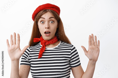 Funny girl mime look surprised as raising hands, leaning on invisible wall during pantomime performace, wearing red beret and scarf, white background